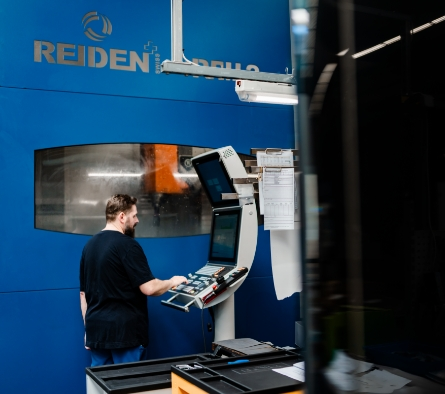 Ein Mann bedient eine Maschine in einer Produktionshalle mit einer blauen Wand und einem Logo.