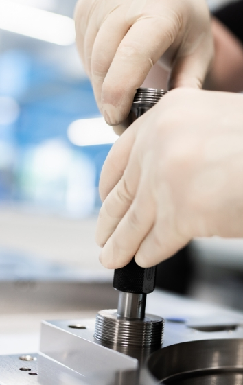 Hände mit Handschuhen montieren ein mechanisches Teil auf einer Werkbank.