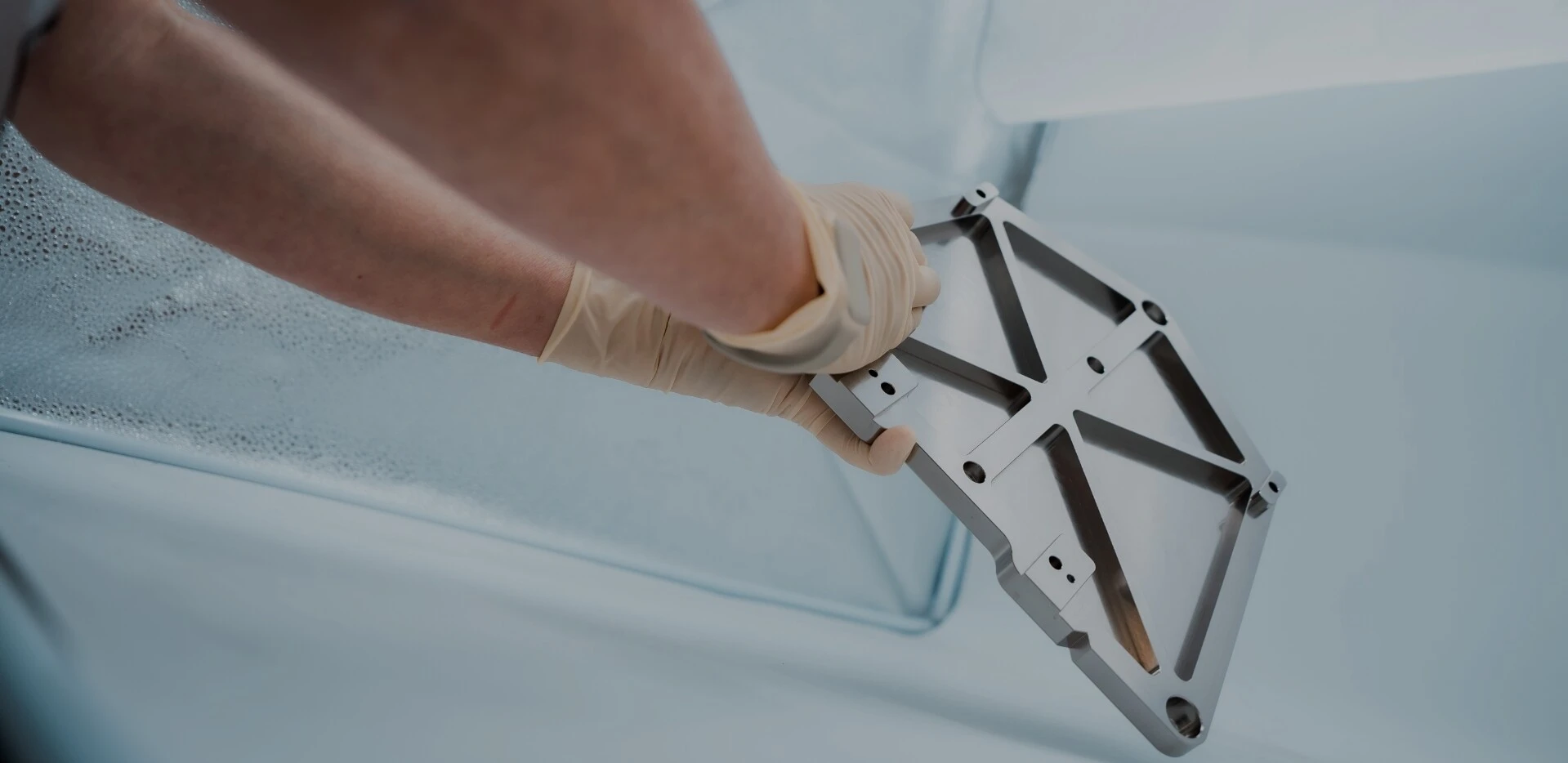 Ein Hand, das eine metallische Montagehalterung mit einer strukturierten Oberfläche hält, während sich Blasen auf einer glatten Oberfläche im Hintergrund befinden.