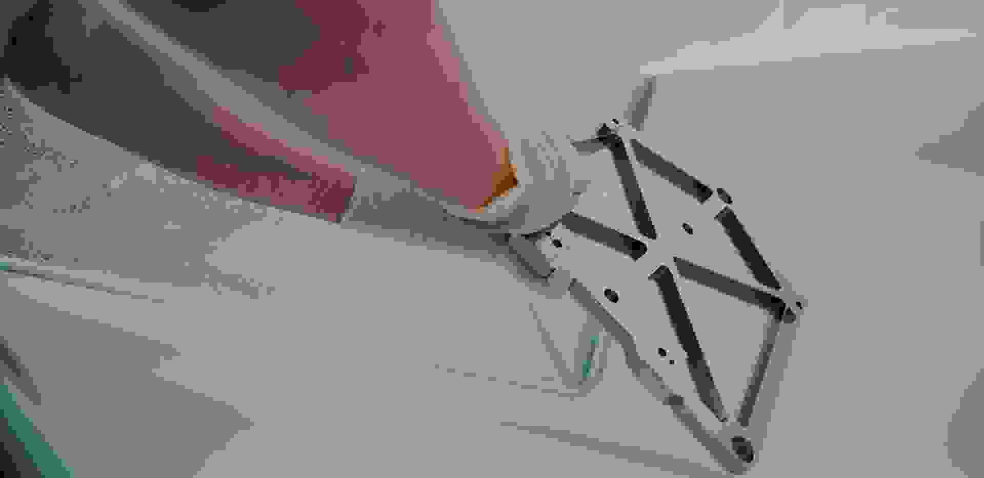 Ein Hand, das eine metallische Montagehalterung mit einer strukturierten Oberfläche hält, während sich Blasen auf einer glatten Oberfläche im Hintergrund befinden.