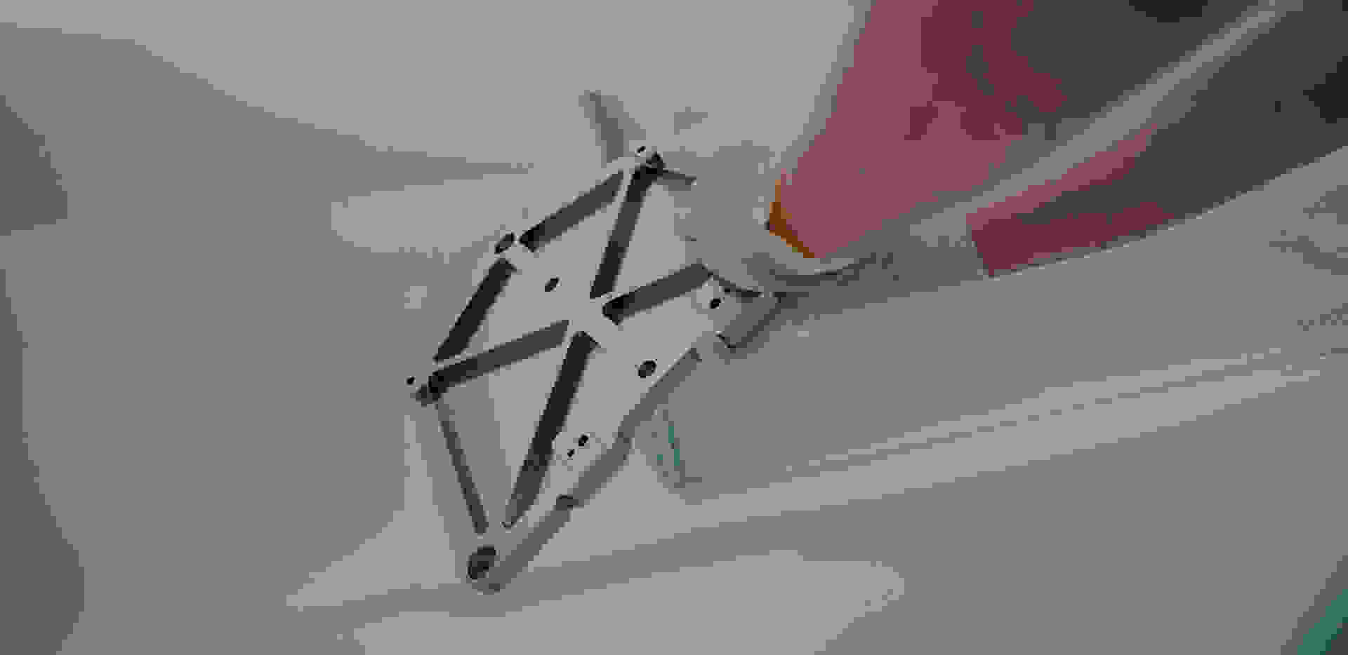 Eine Hand hält ein silbernes, metallisches Bauteil mit einer komplexen Form, während es in einem sauberen Umfeld präsentiert wird.