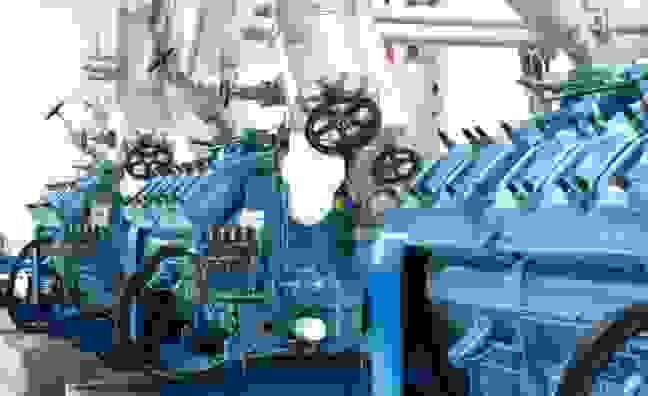 Eine Reihe von blauen Motoren mit Rohren und Ventilen in einer Industrieumgebung.