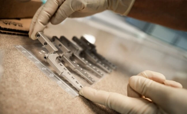 Ein Handwerker sortiert chirurgische Instrumente auf einem Tisch. Handschuhe werden getragen.