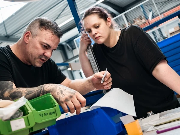 Zwei Personen arbeiten in einer Industrieumgebung, Blick auf eine Arbeitsfläche mit Werkzeugen und Materialien.