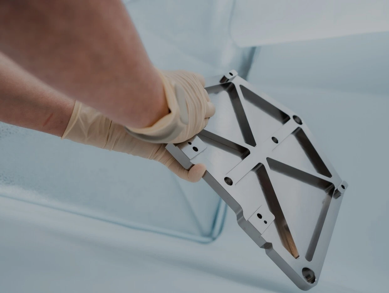 Ein Hand, das eine metallische Montagehalterung mit einer strukturierten Oberfläche hält, während sich Blasen auf einer glatten Oberfläche im Hintergrund befinden.