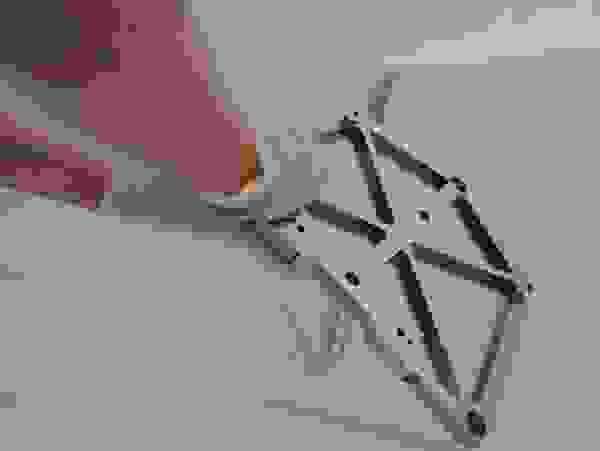 Ein Hand, das eine metallische Montagehalterung mit einer strukturierten Oberfläche hält, während sich Blasen auf einer glatten Oberfläche im Hintergrund befinden.