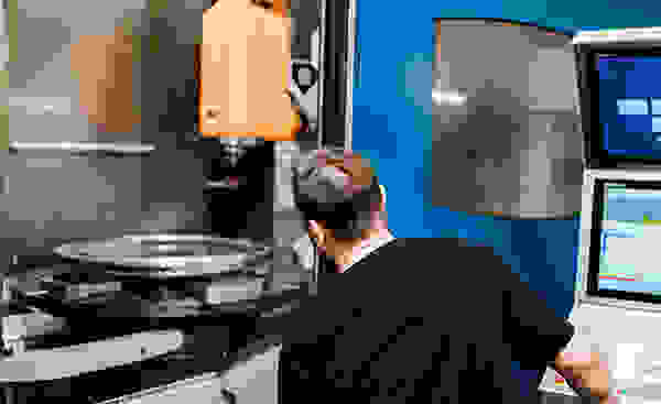 Eine Maschinenbearbeitung mit einem Werkzeug, das einen zylindrischen Metallteil fräst. Helles Licht und reflektierende Oberflächen sind sichtbar.